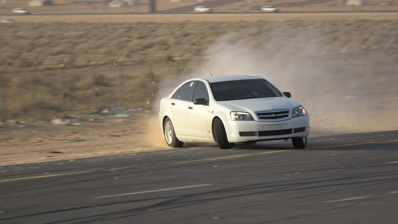White sedan drifting on asphalt with dust trail behind.
