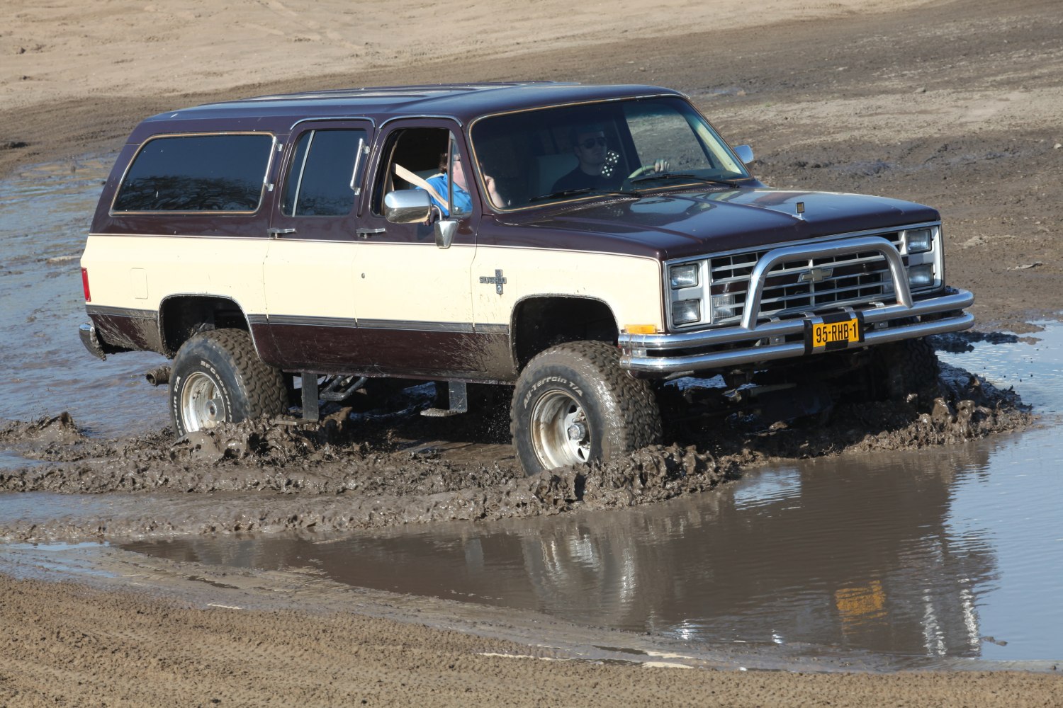 Full-size SUV with raised suspension and bull bar driving through muddy terrain.
