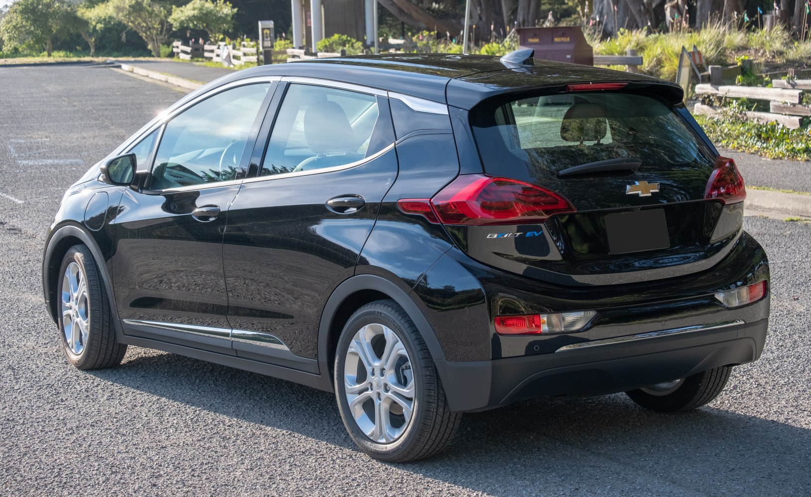 Rear side view of black compact electric hatchback with visible taillights and roof spoiler
