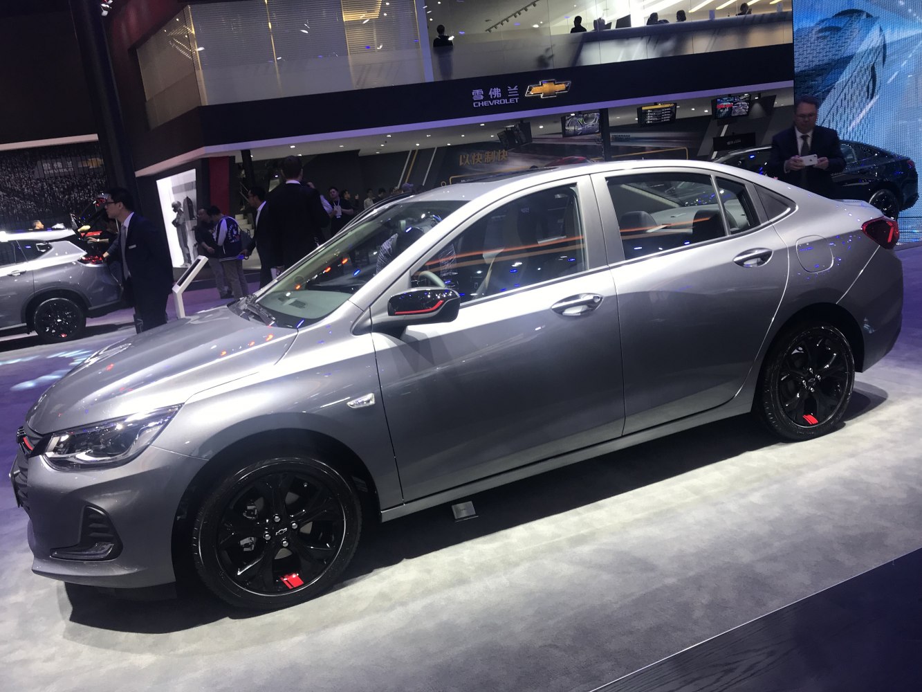 Gray sedan with black alloy wheels and sporty mirror trim in showroom.