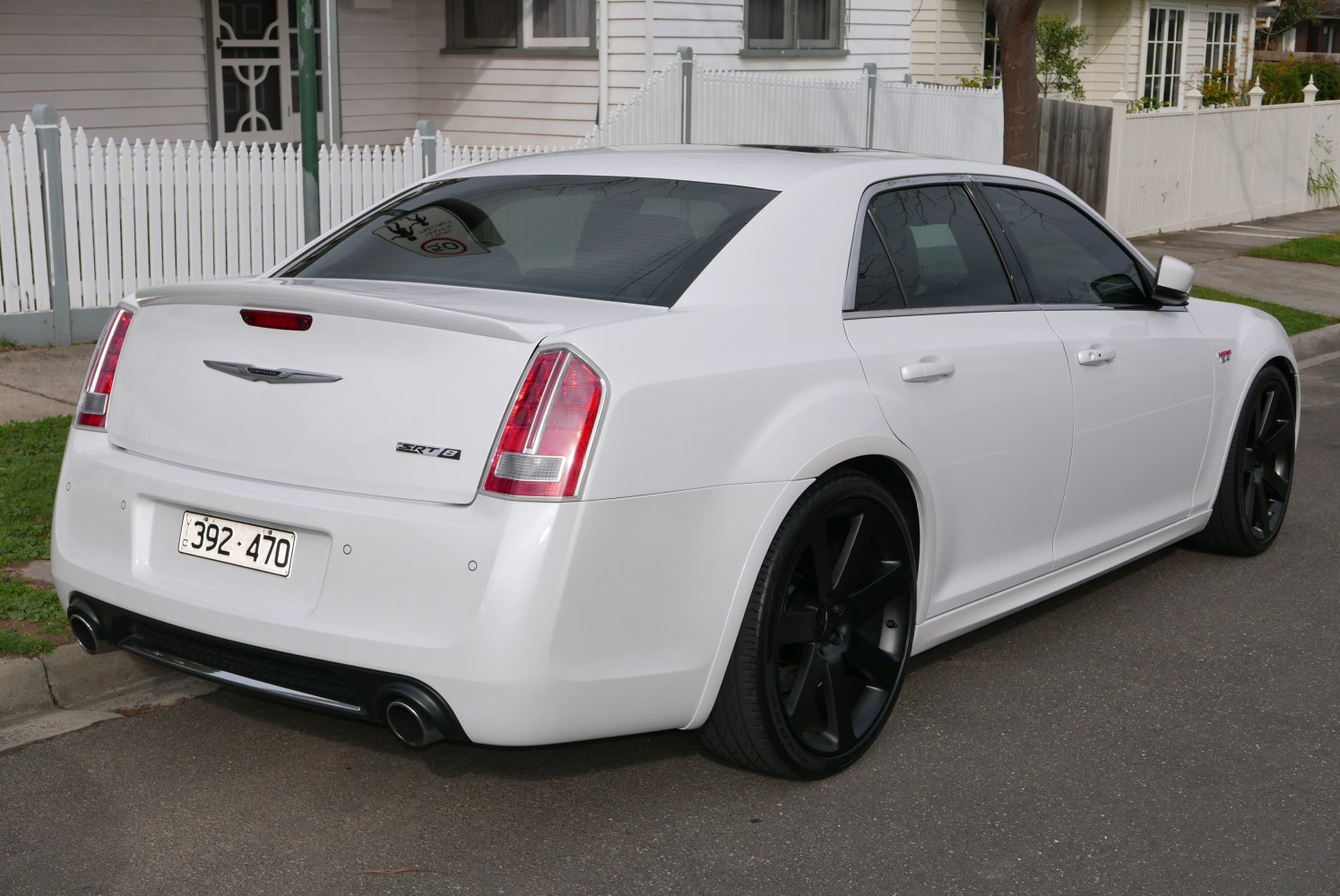 White sedan rear side with black wheels, dual exhaust, rear spoiler
