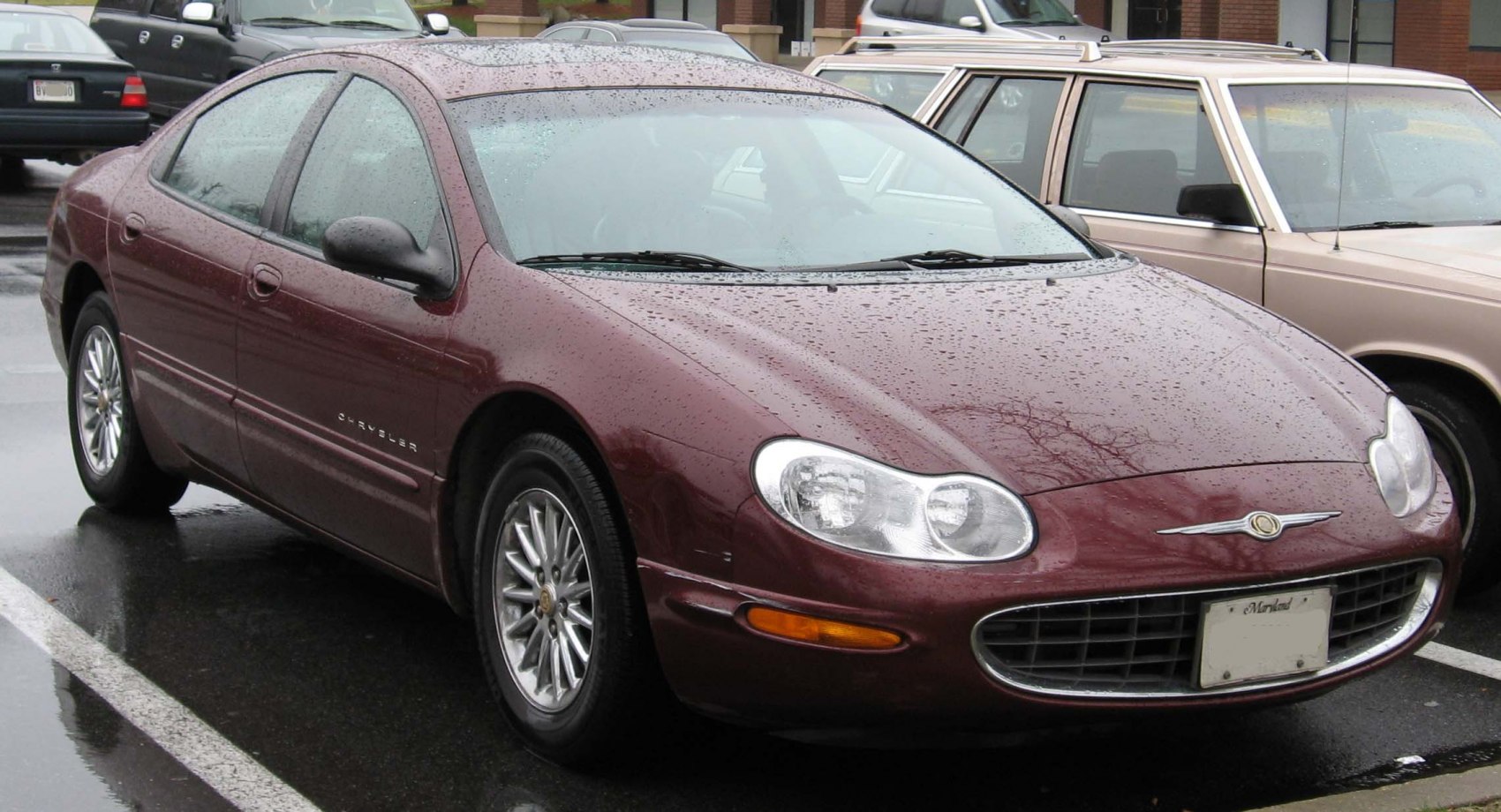 Front grille and side profile of a maroon sedan with rain droplets