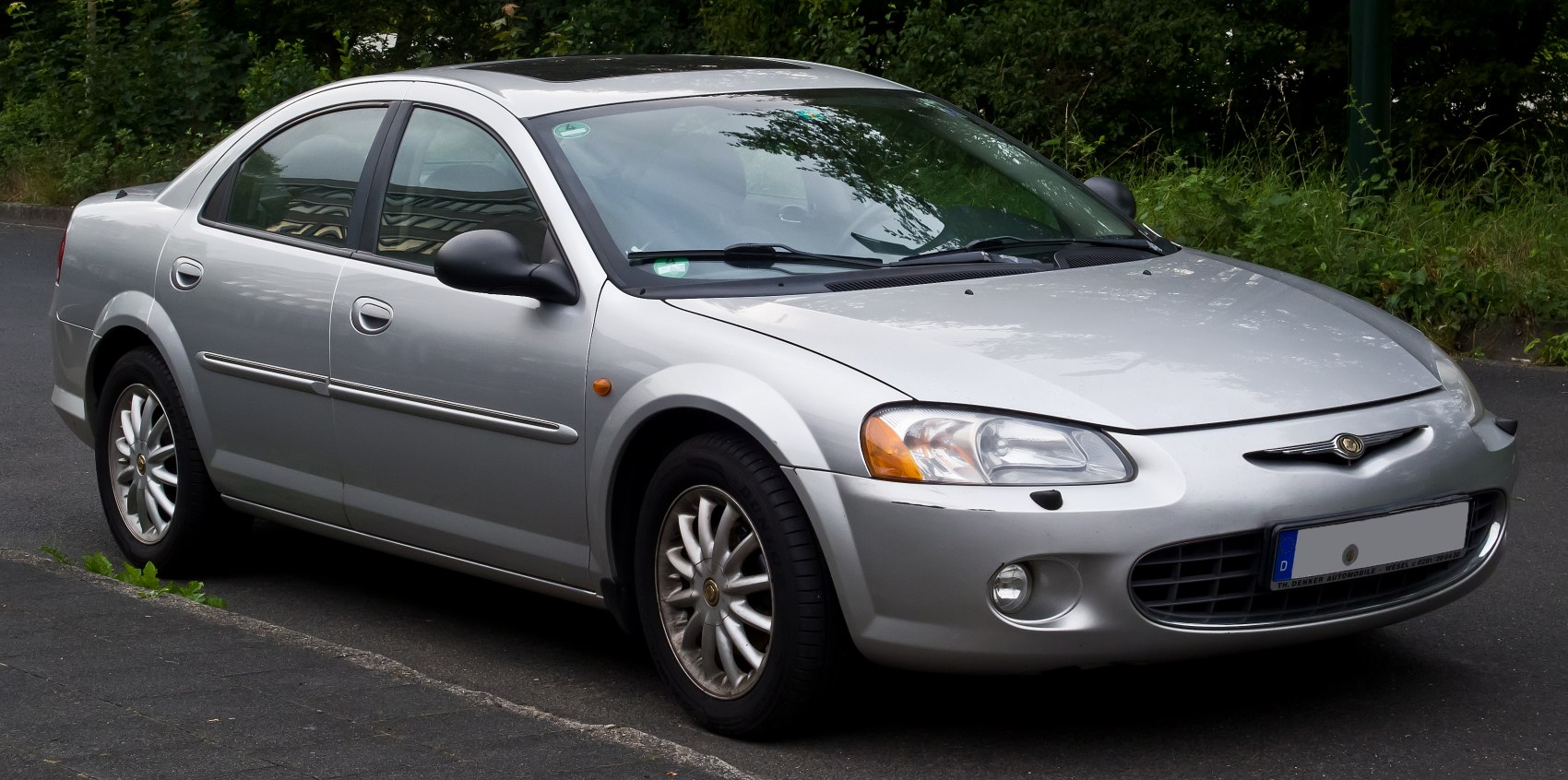 Silver four-door sedan front side view with round headlights and multi-spoke wheels