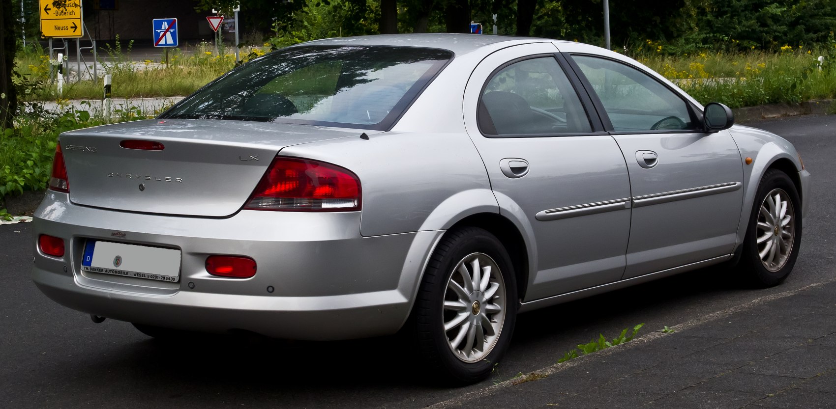 Silver mid-2000s sedan rear side with alloy wheels and taillights