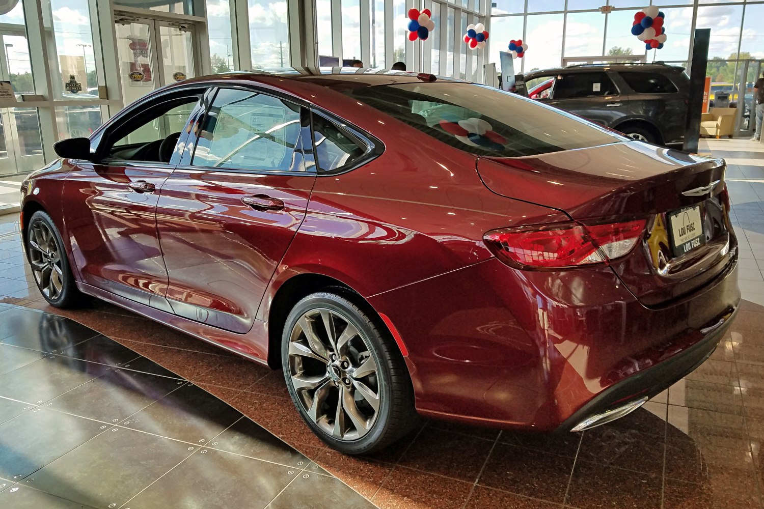Rear side view of red sedan with alloy wheels in a bright showroom