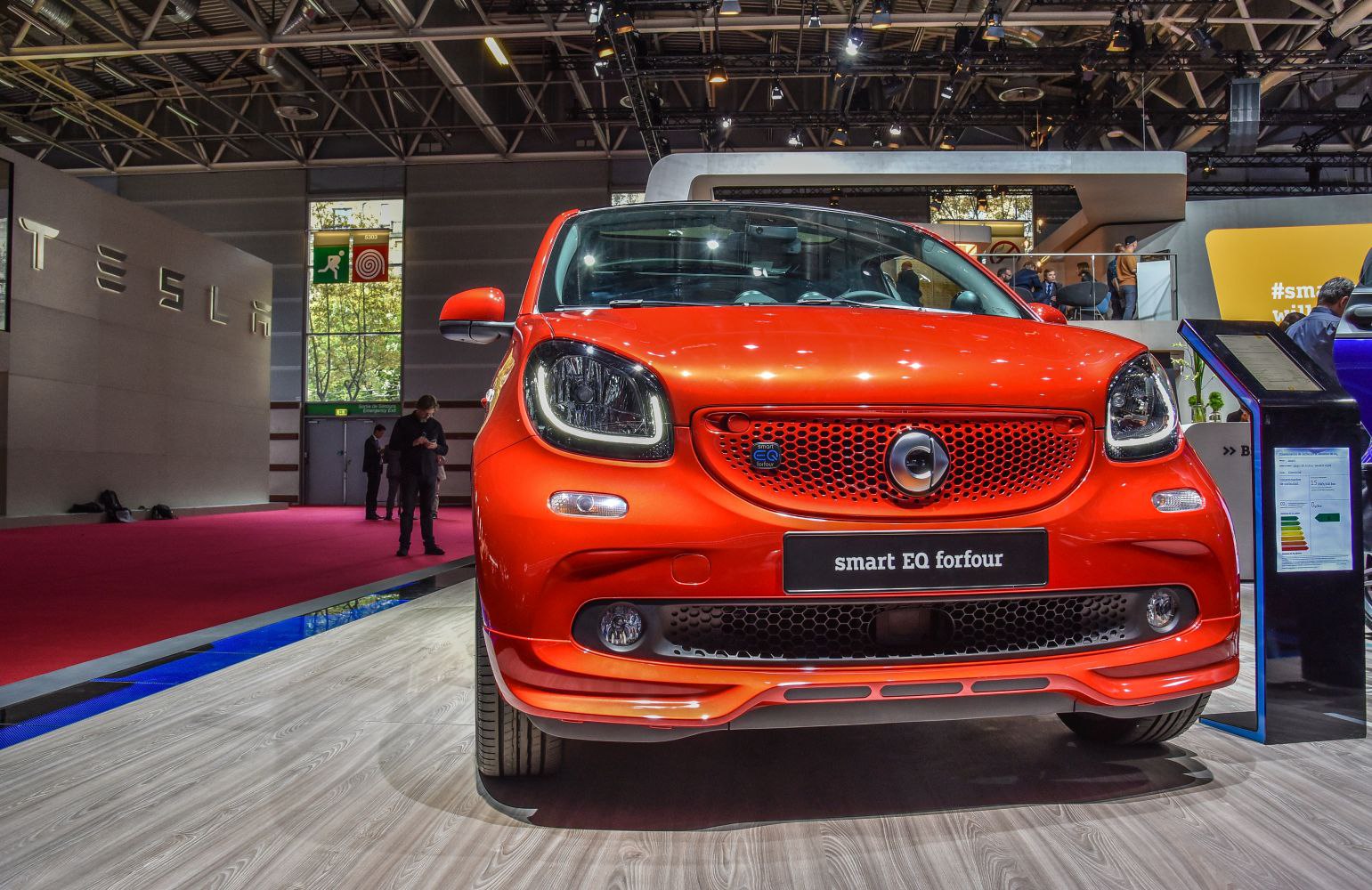 Close-up front view of vibrant orange compact electric car with modern headlights.