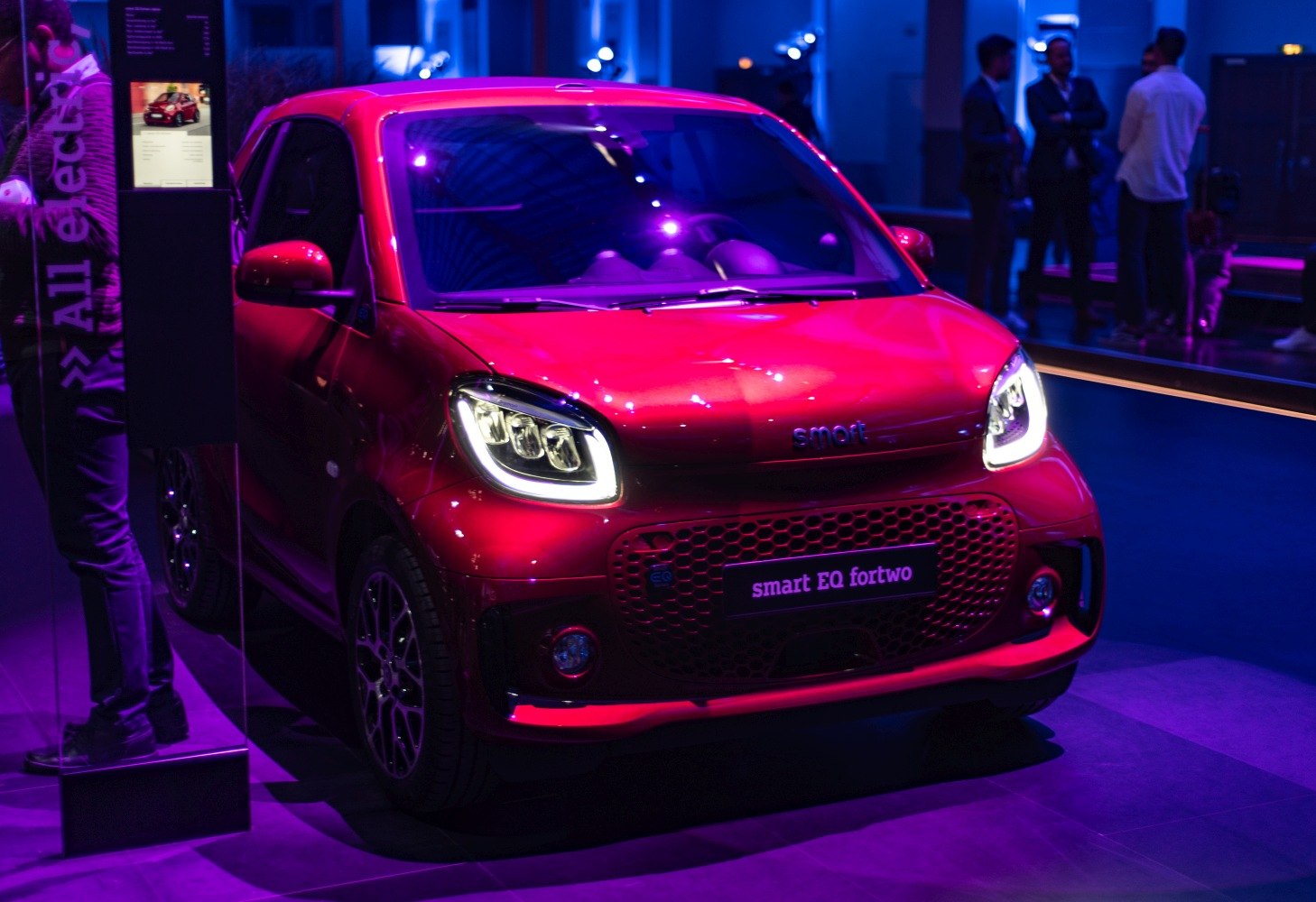 Front view of a red electric city car with modern headlights and honeycomb grille