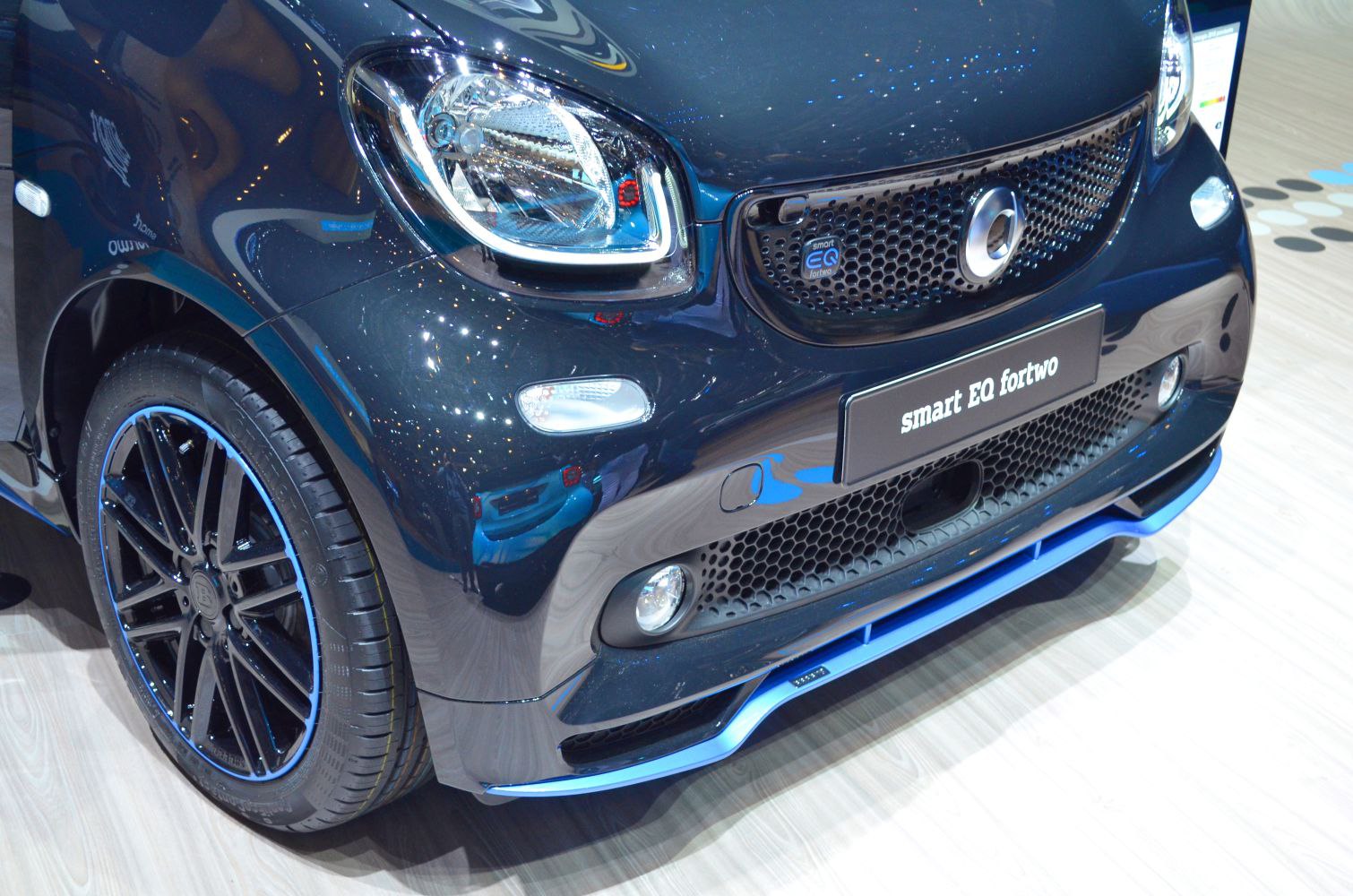 Close-up of front end with headlight, grille, and black alloy wheels with blue trim.