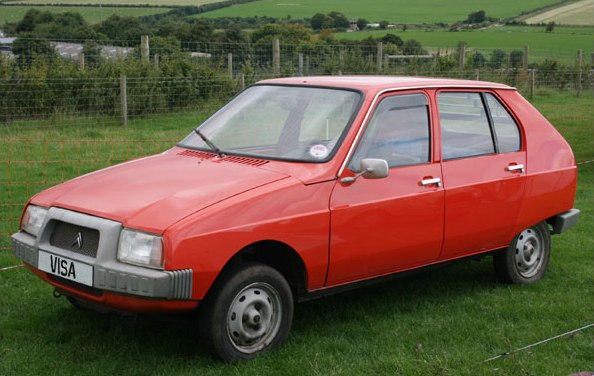 Orange compact four-door hatchback with boxy design parked on grass