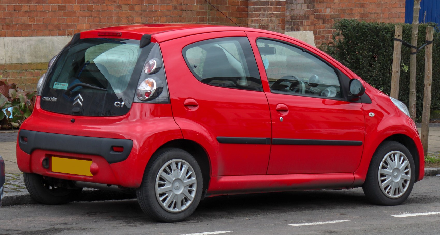 Rear side view of red compact 5-door hatchback with visible tail lights and door handles.
