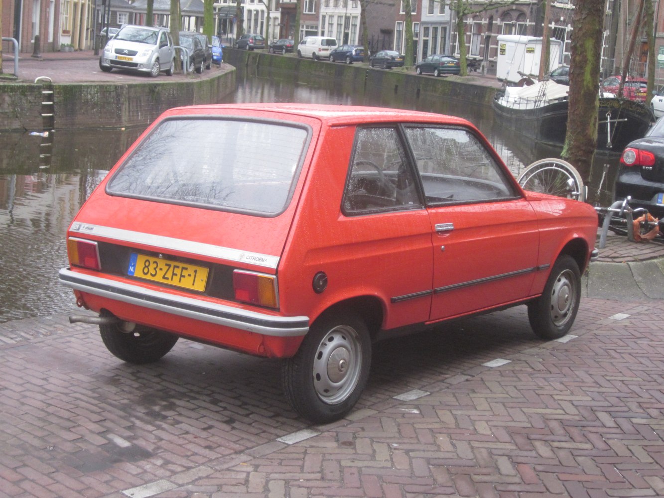 Rear-side view of a red hatchback with chrome bumper and simple wheel covers.