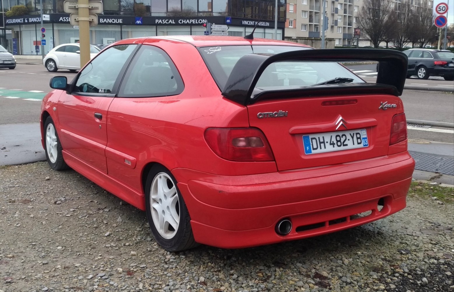 Red compact hatchback with black rear spoiler and white rims