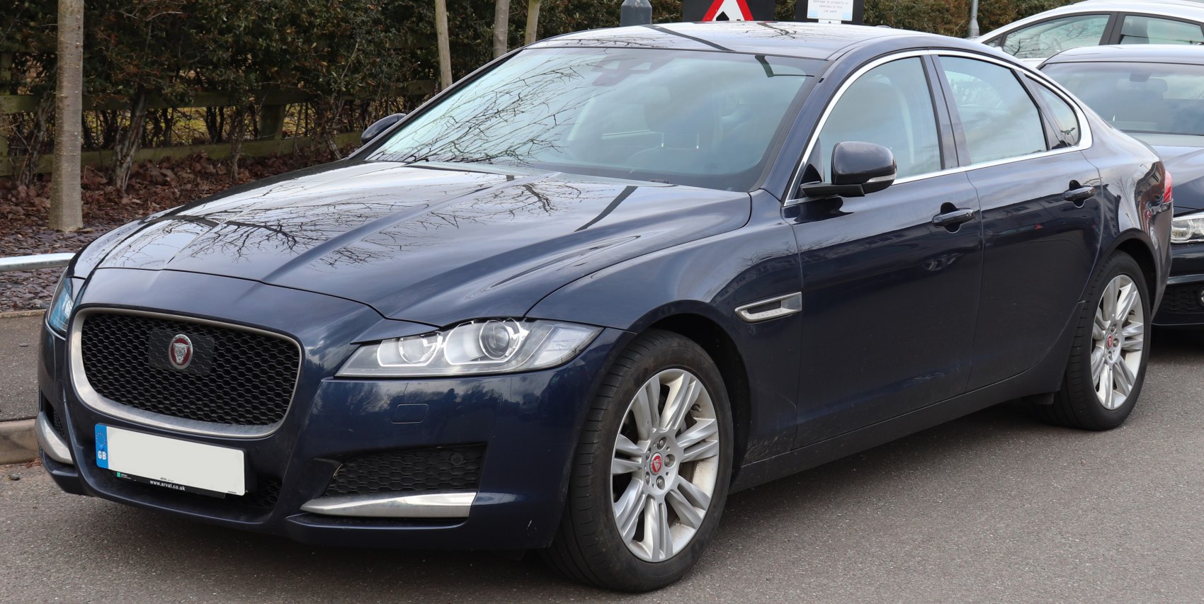 Front three-quarter view of dark-colored luxury sedan with prominent grille and sleek headlights.