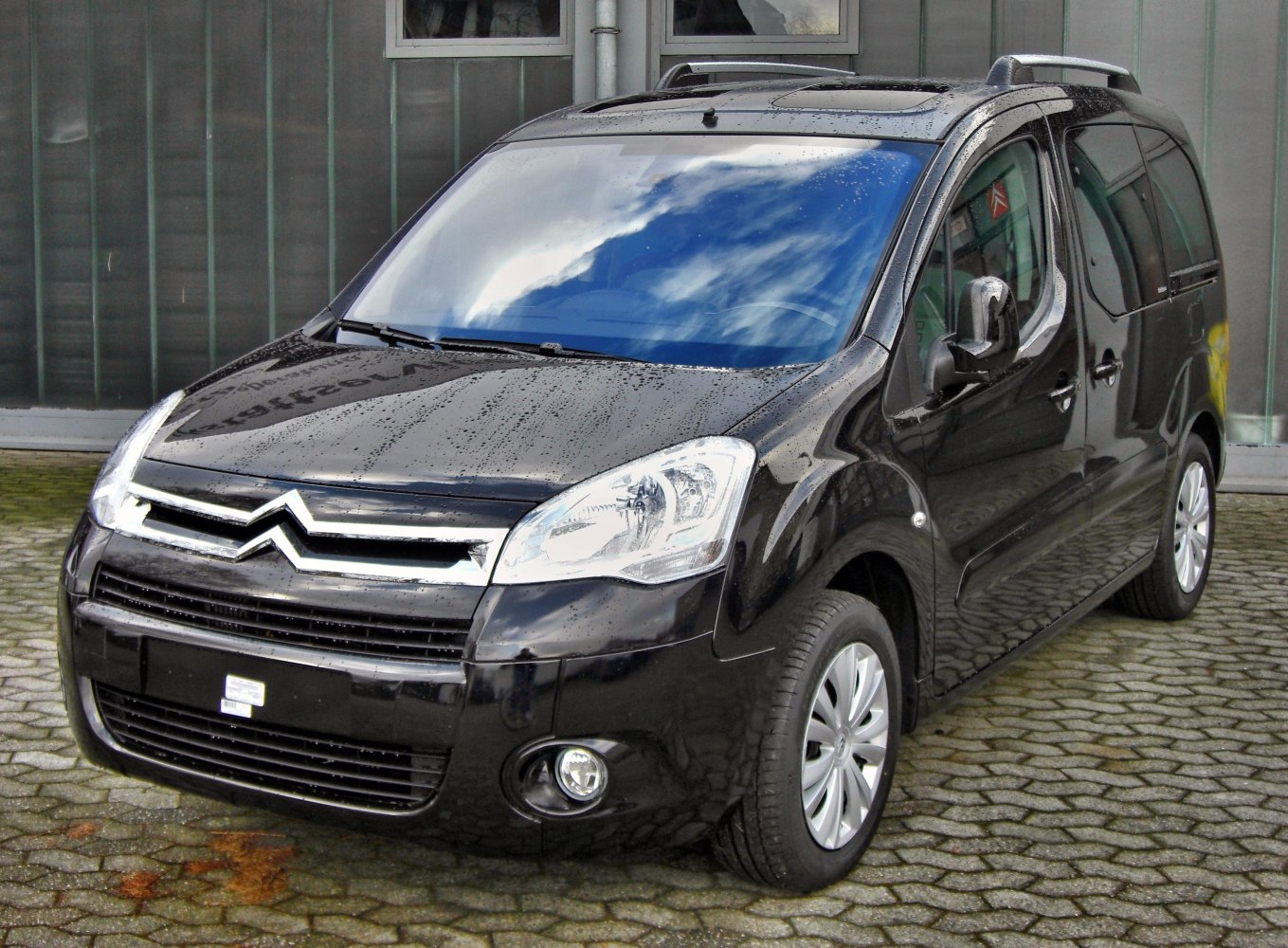 Black multi-purpose van with sliding side door and roof rails, front-side view