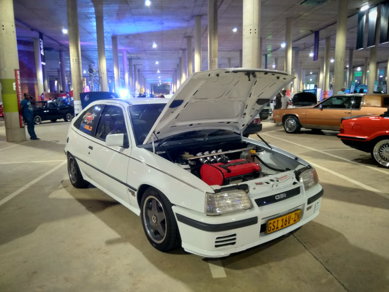 White hatchback with open hood revealing bright red engine.