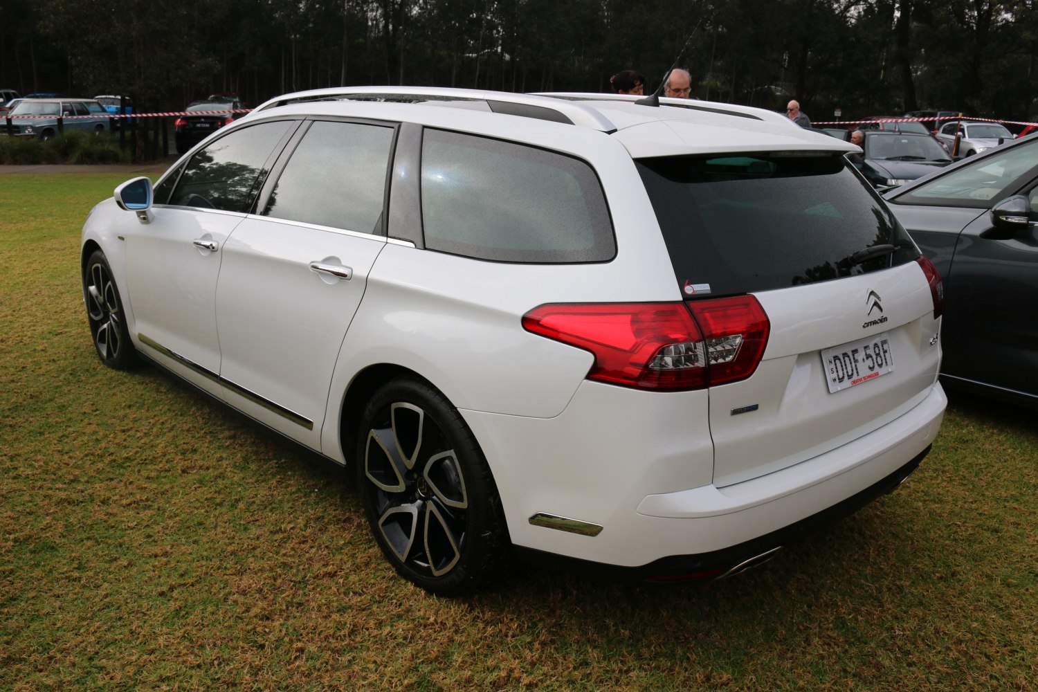 White station wagon with rear lights, roof rails, and dark alloy wheels on grass