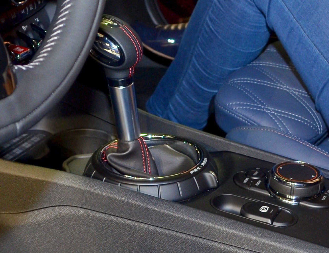 Gear shifter with red stitching and quilted leather seat in car center console.