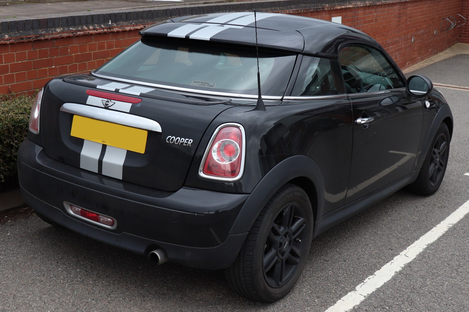 Rear side view of black coupe with white racing stripes and black wheels