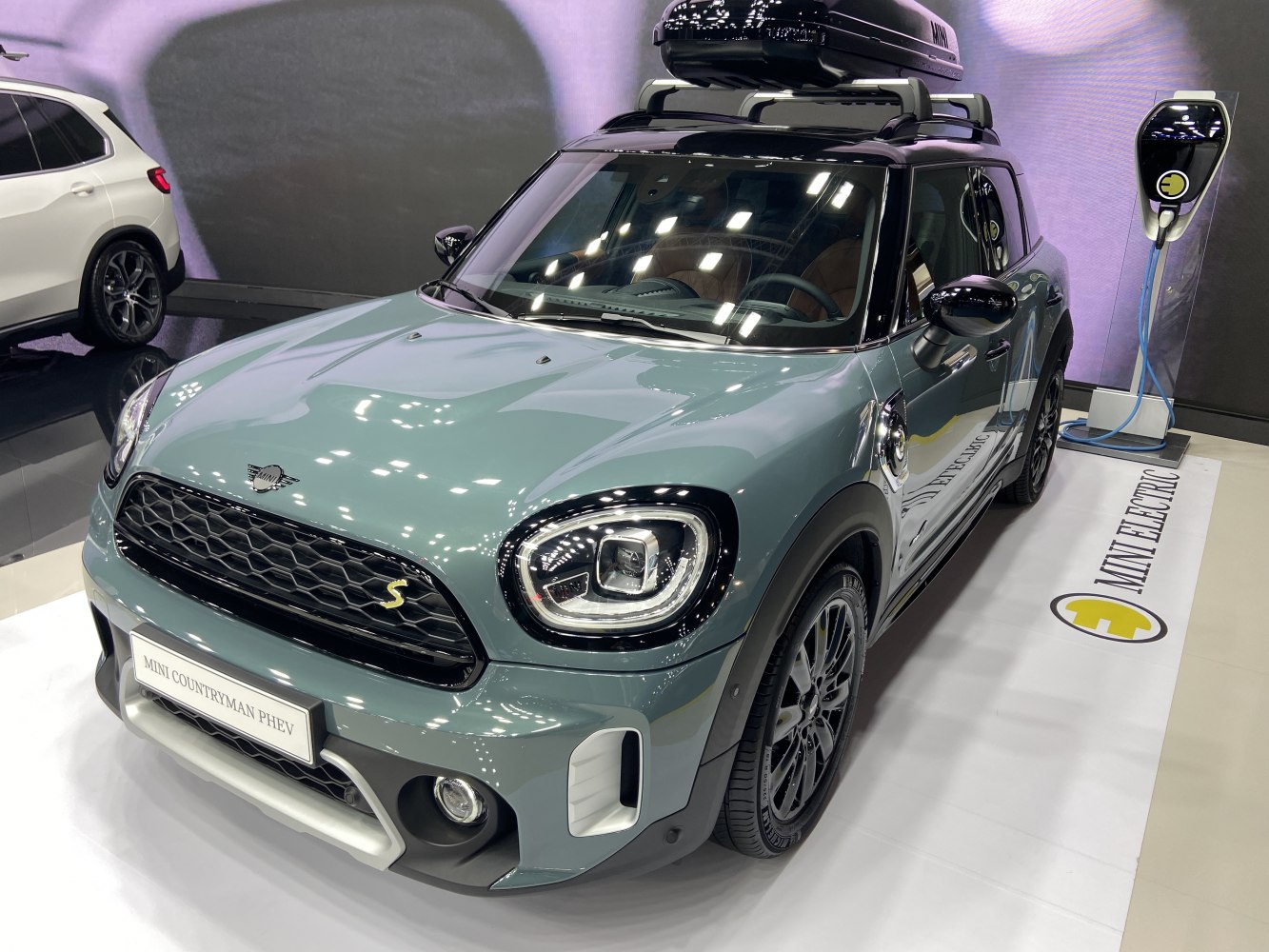 Front view of a Mini Countryman with roof box and electric charging station