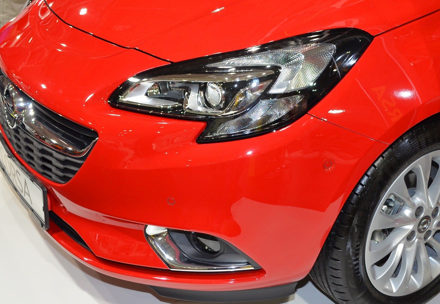Close-up of front headlight, grille, and alloy wheel of a red modern hatchback.