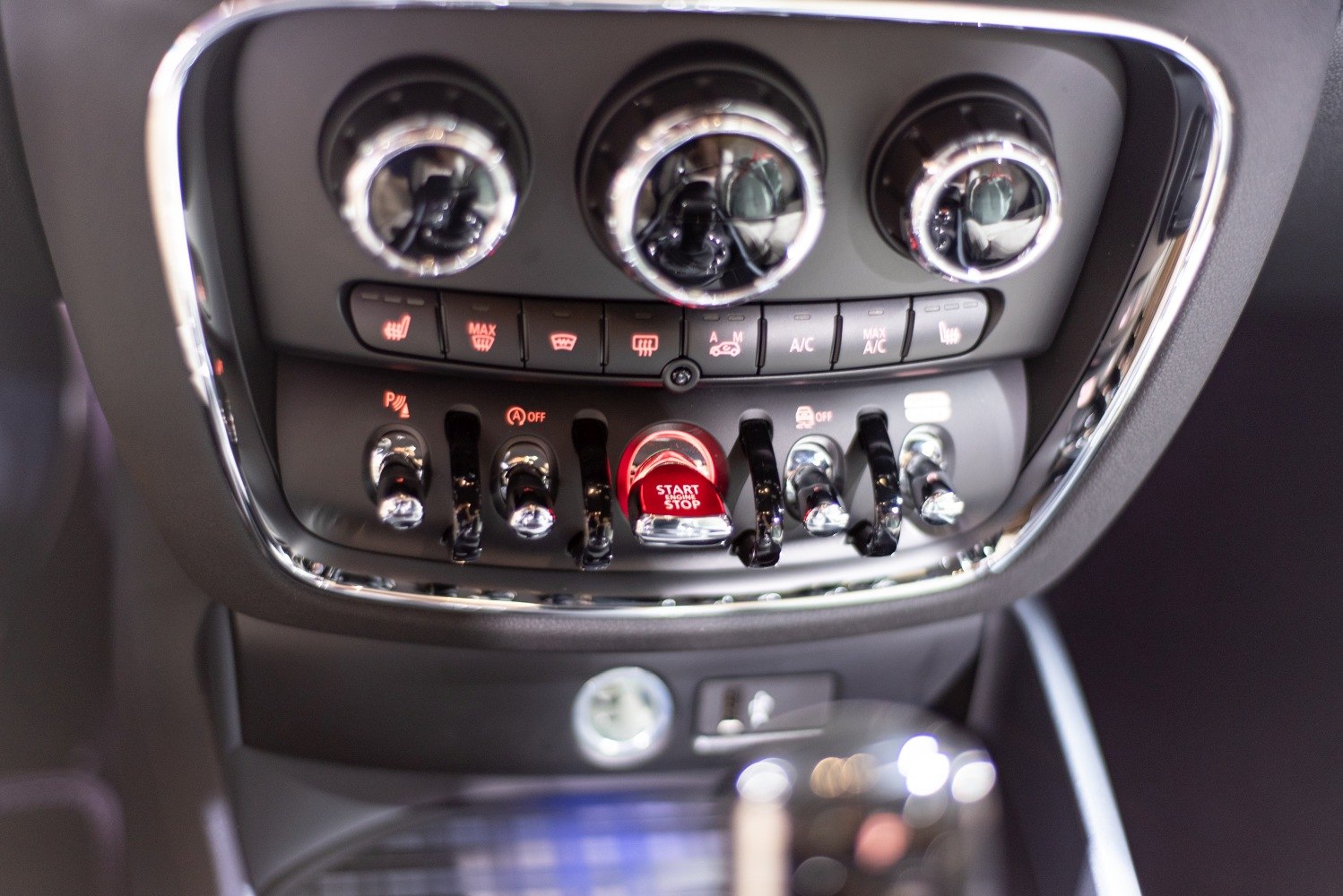 Close-up view of car climate controls and chrome toggle switches with illuminated start stop button.