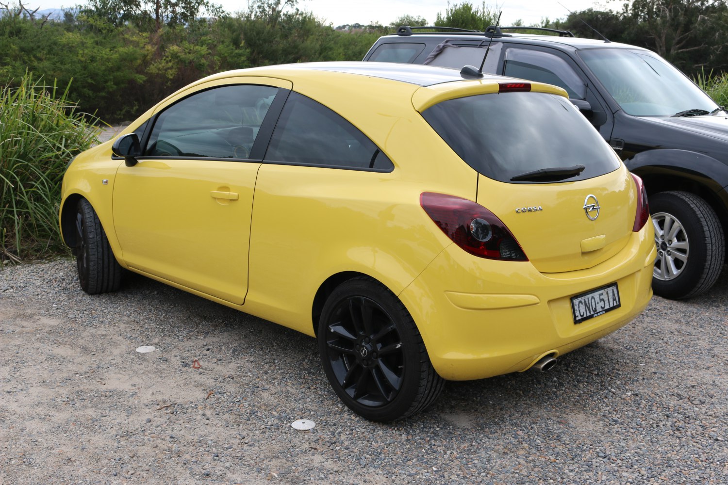 Yellow hatchback 3-door with black wheels rear side shot