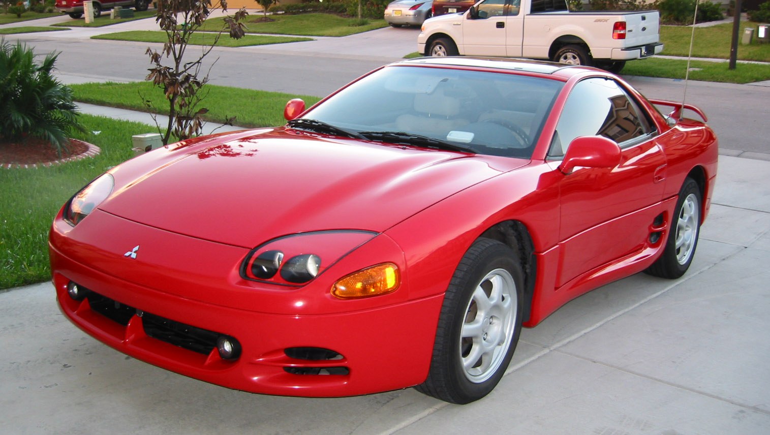 Red sporty coupe front and side view with distinct headlights and aerodynamic body.