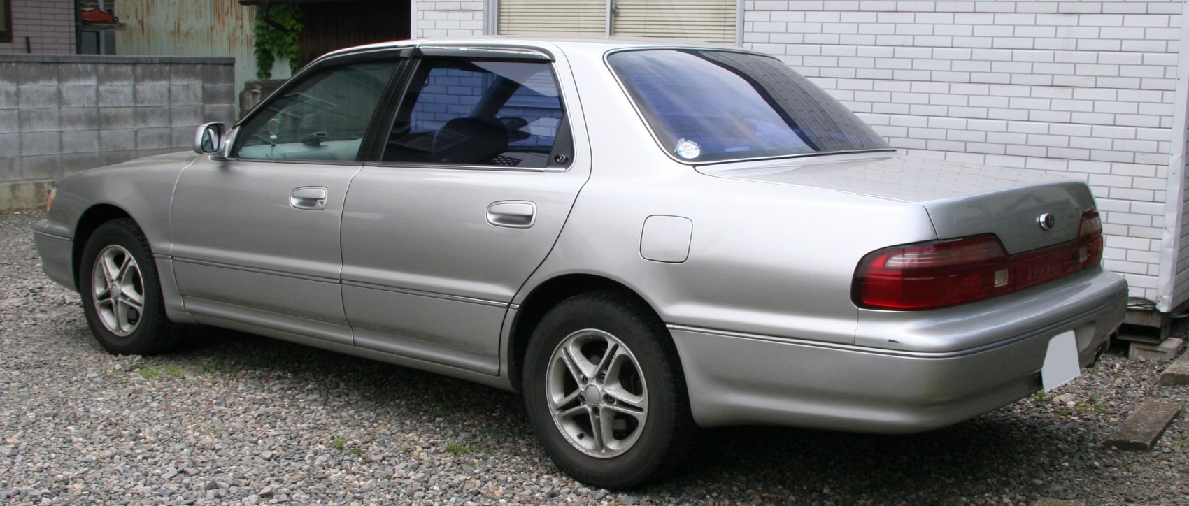 Silver sedan with distinctive taillights and alloy wheels parked on gravel.