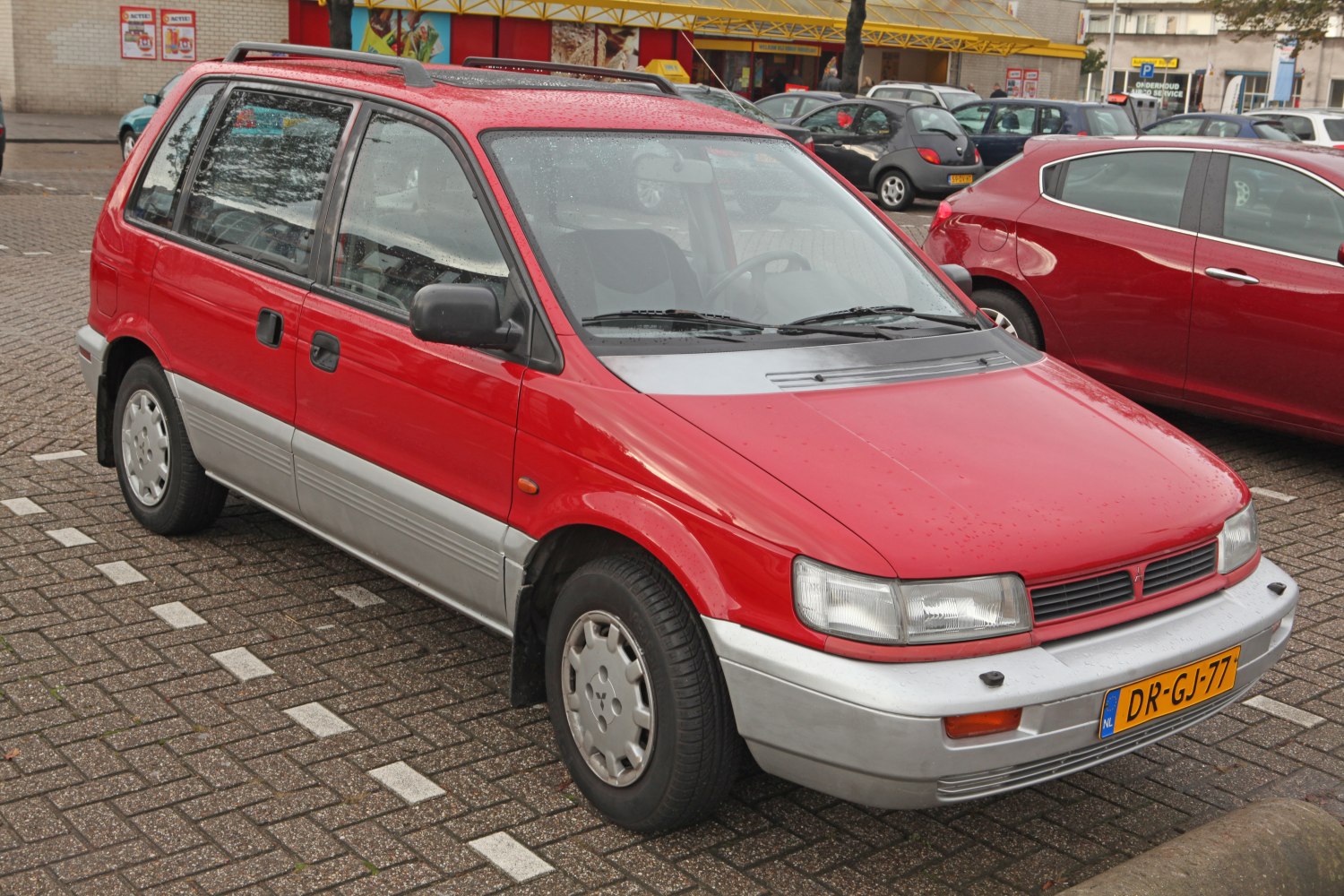Red compact hatchback with two-tone bumper and roof rails