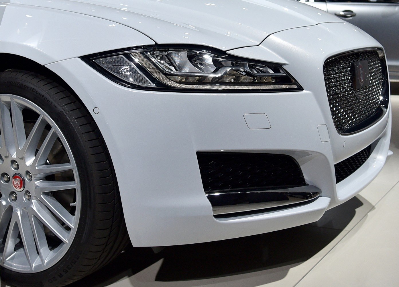 Closeup of front headlight and mesh grille on white luxury sedan