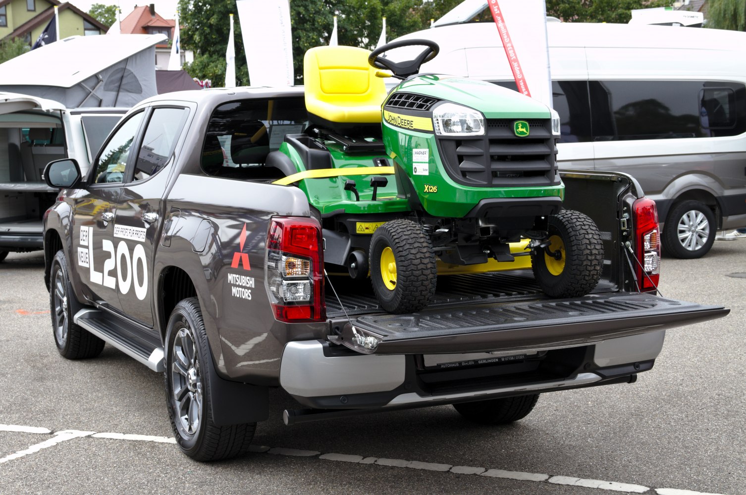Pickup truck with open bed carrying a green yellow John Deere ride-on mower
