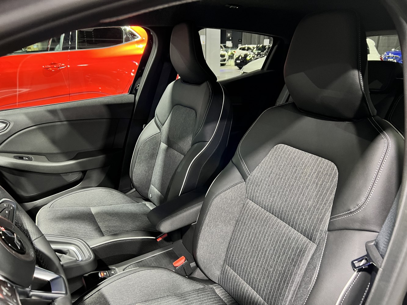 Cloth and leather front seats with detailed stitching and armrest in a modern vehicle interior.