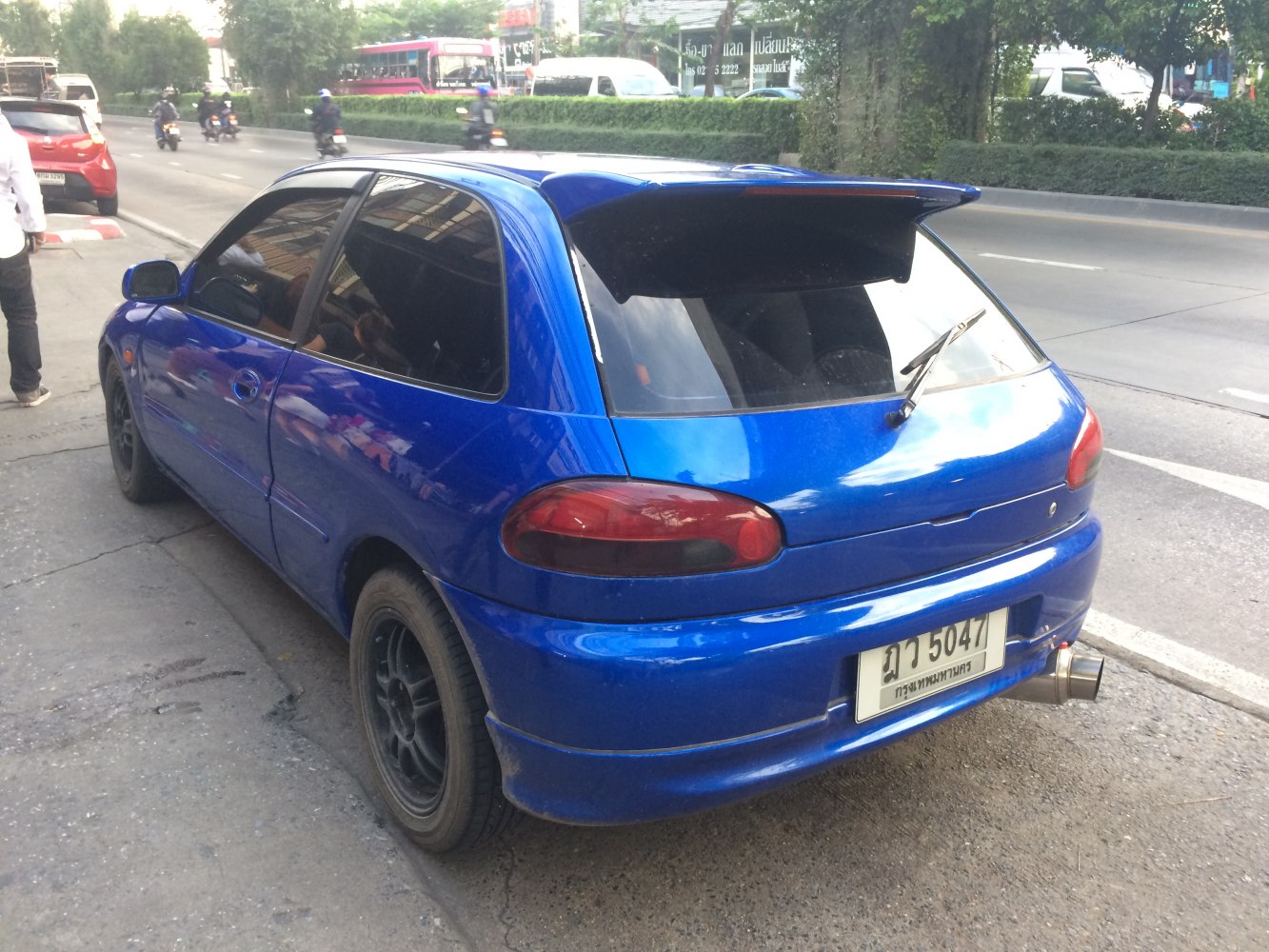 Blue hatchback with rear spoiler, sporty exhaust, black wheels, tinted windows