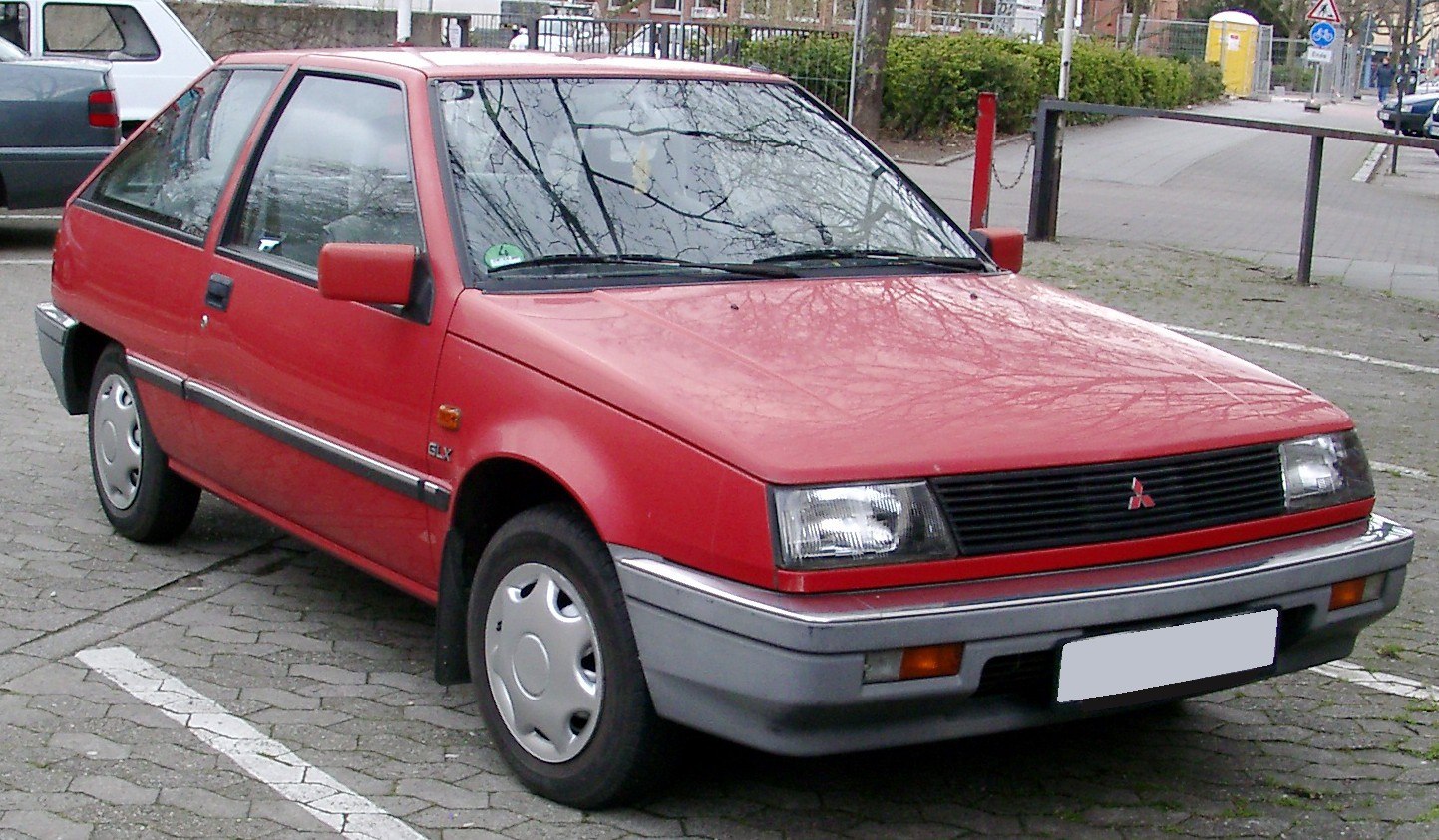 Red vintage hatchback, rectangular headlights, black grille, hubcap wheels