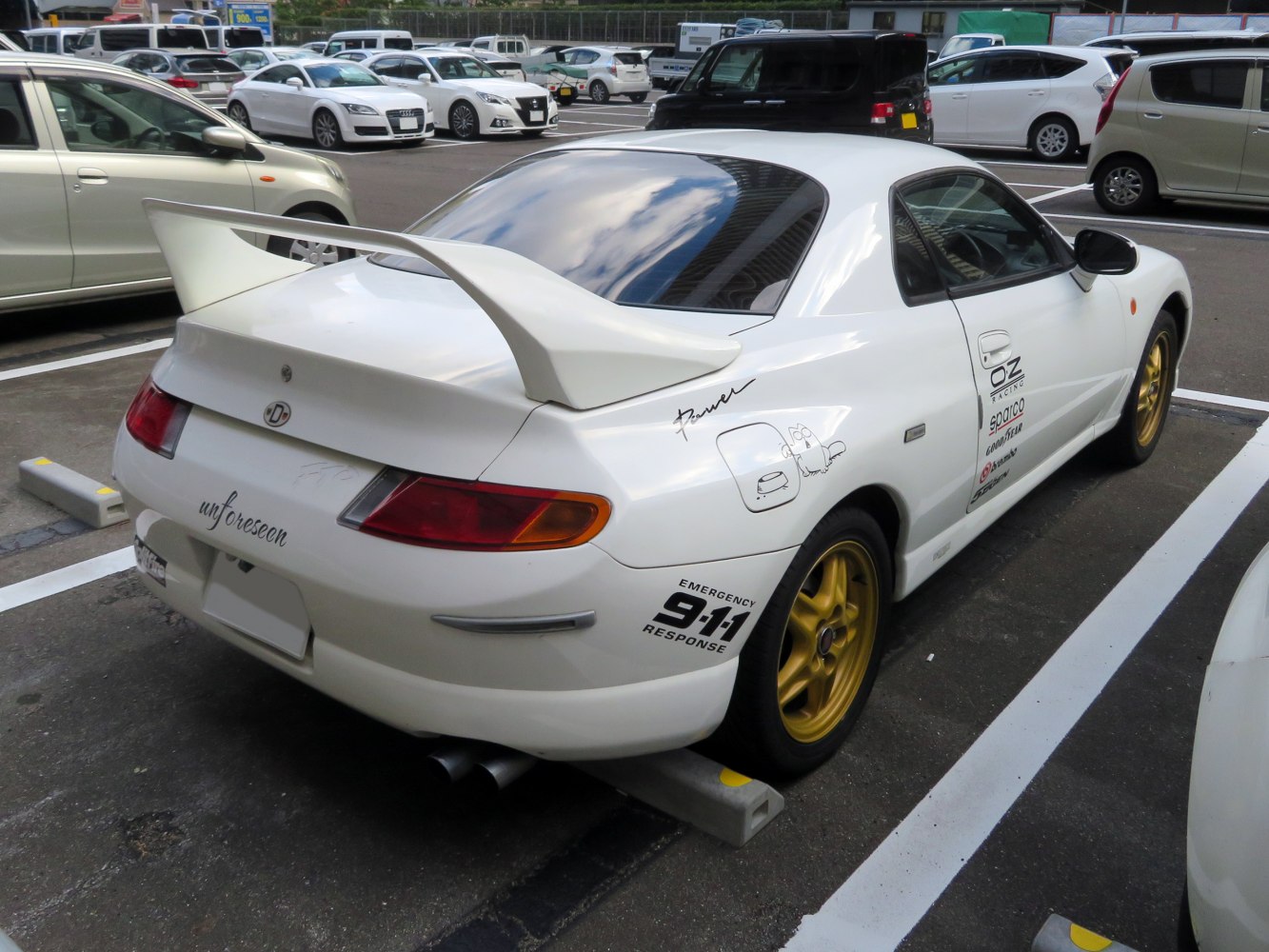 White coupe with large rear wing spoiler and gold alloy wheels