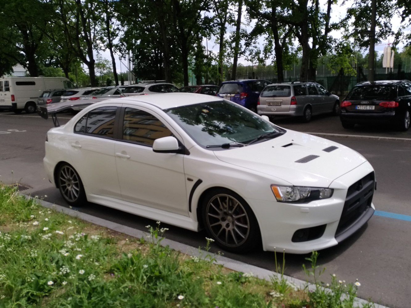 White performance sedan with large rear spoiler and front hood vents
