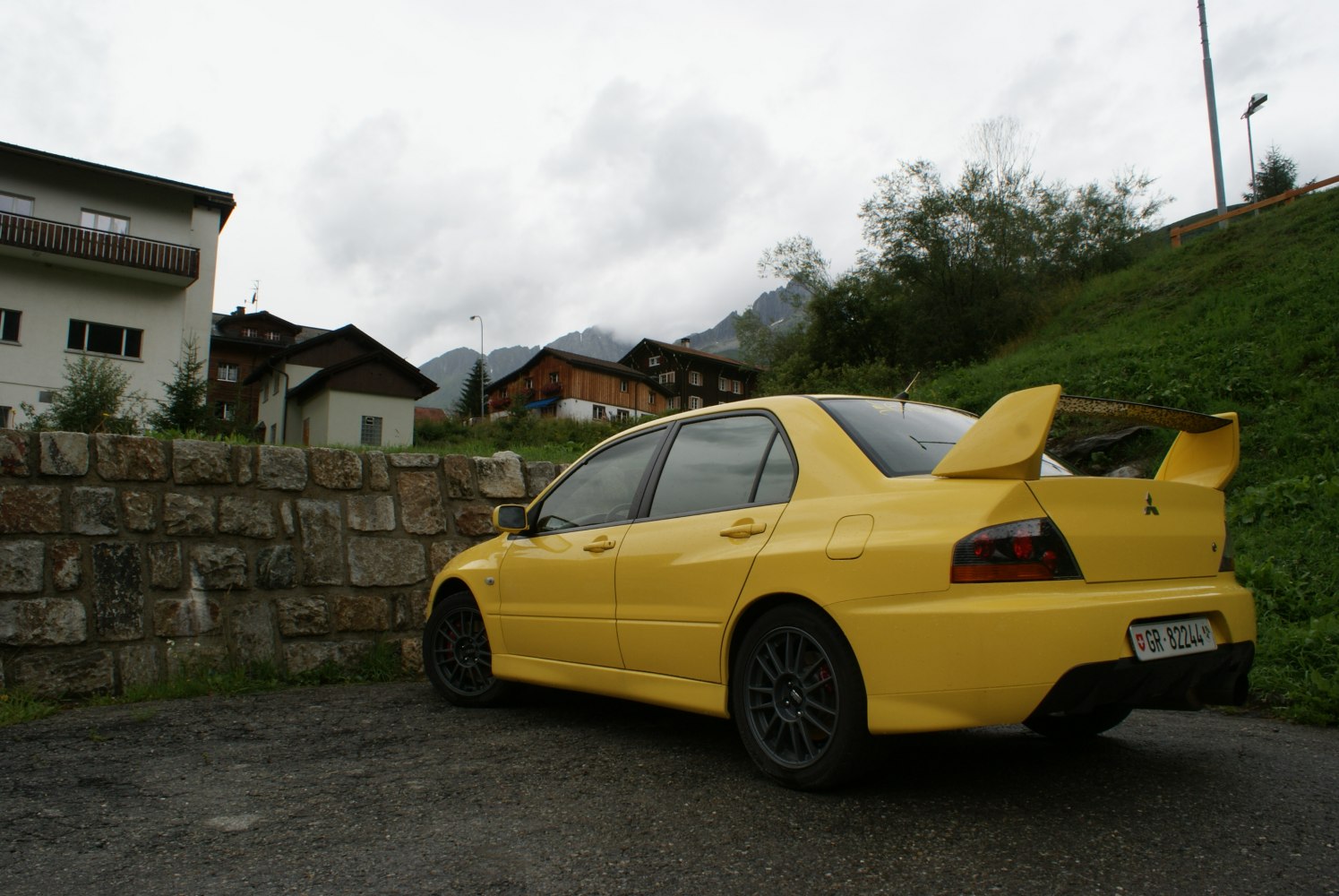 Yellow sedan rear side with large rear wing and black sport wheels