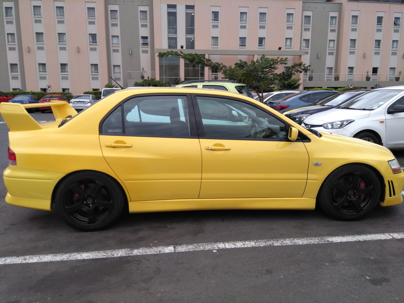 Yellow sports sedan with large rear spoiler and black alloy wheels.