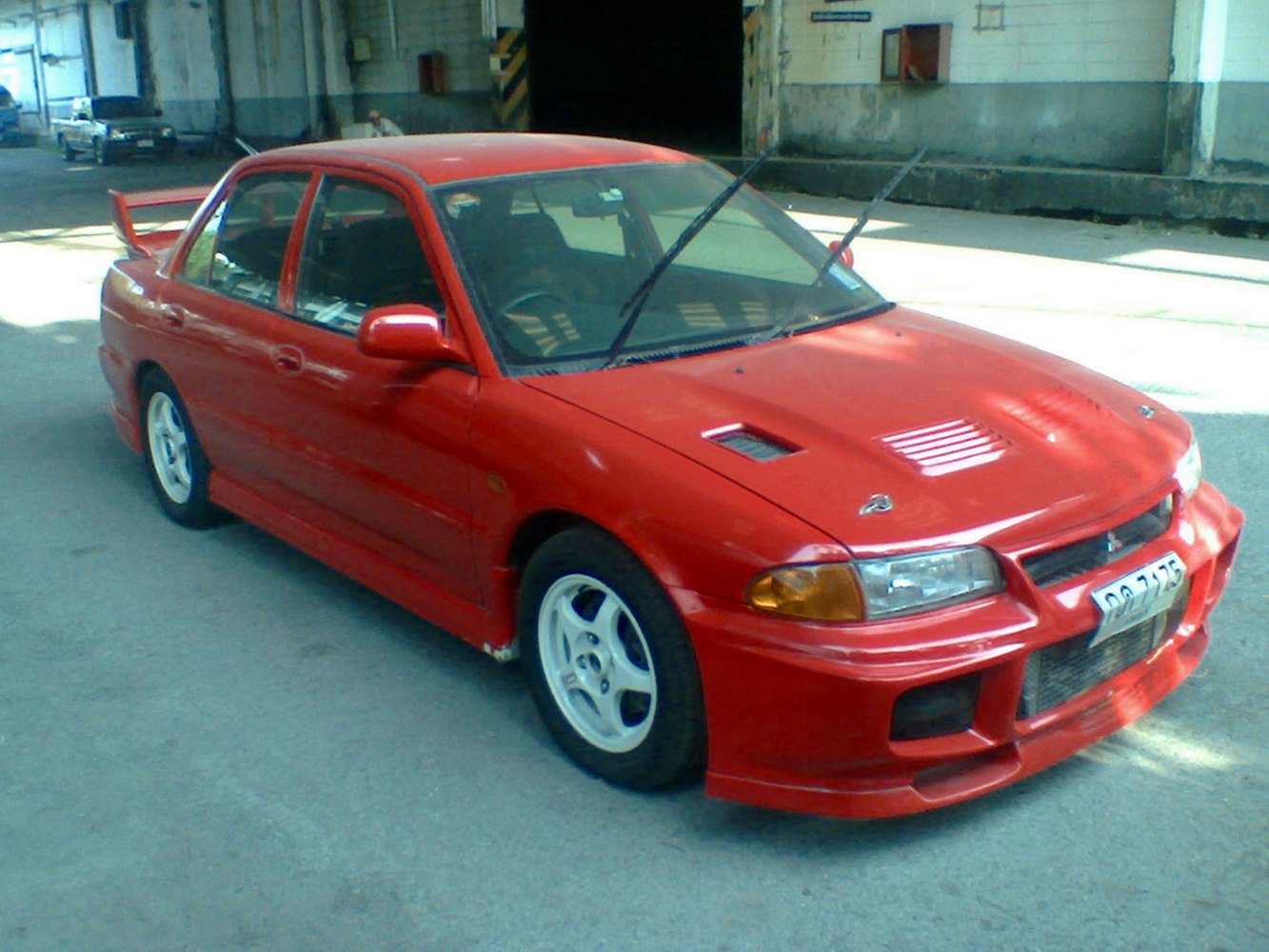Red sedan with hood vents and large rear wing, sporty front bumper and white wheels.