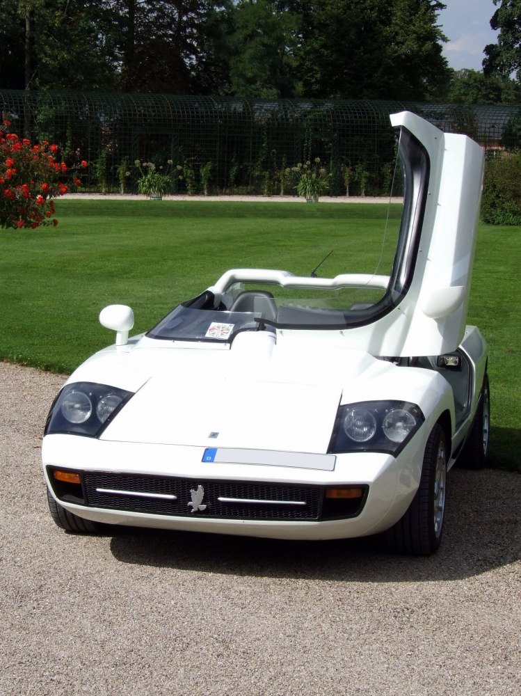 White sports car with one gullwing door open and distinctive dual headlamps