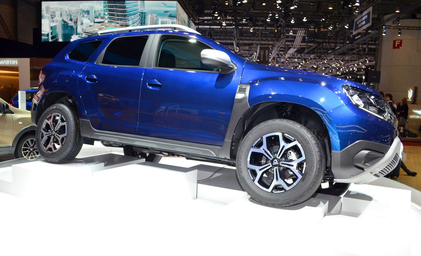 Side view of SUV on stepped white platform with visible wheel details.