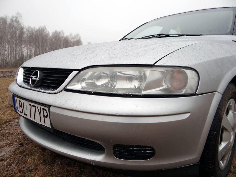 Front headlight and grille close-up with raindrops on hood and bumper