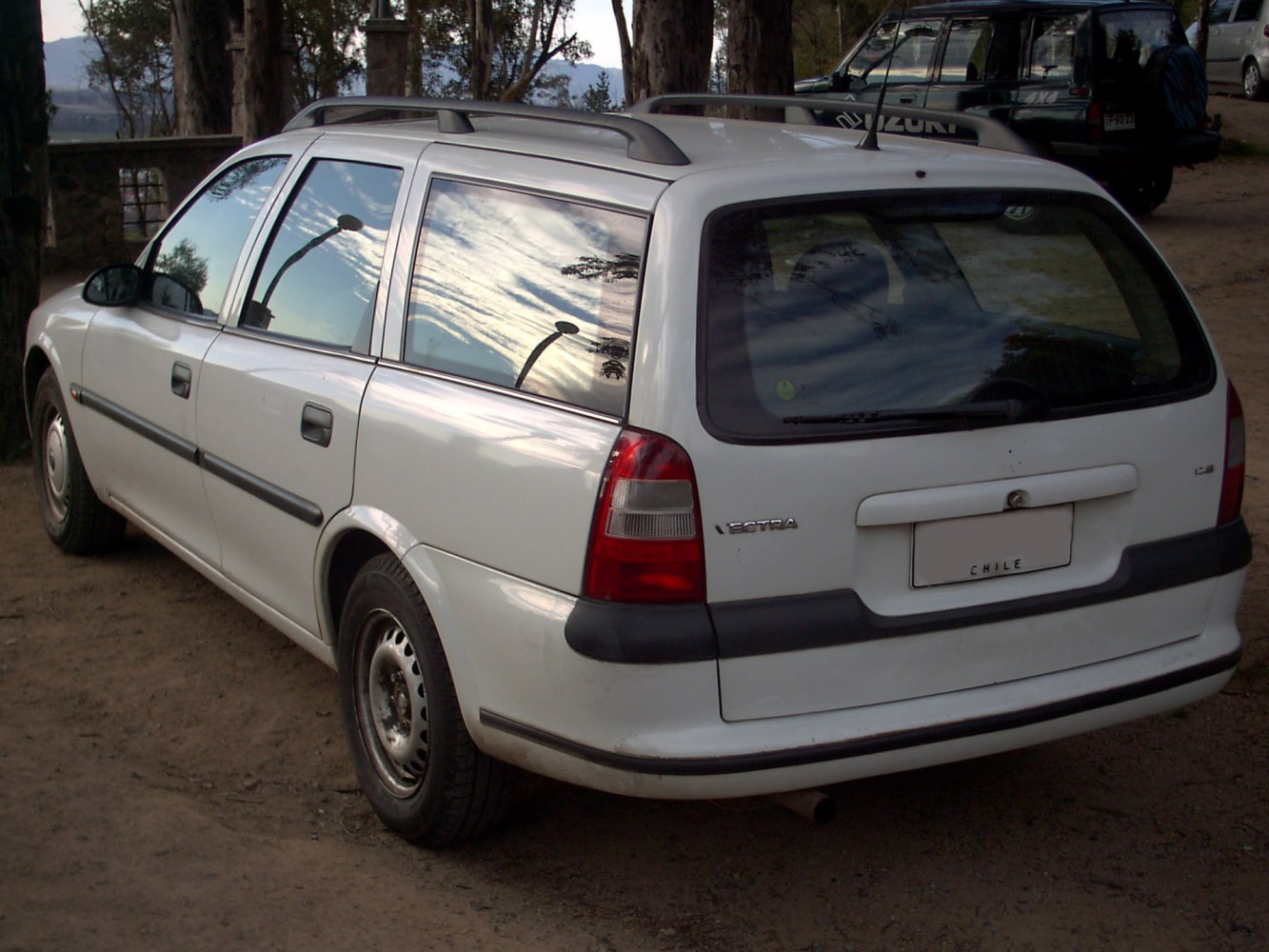 Rear-side view of white wagon with roof rails and tail lights.