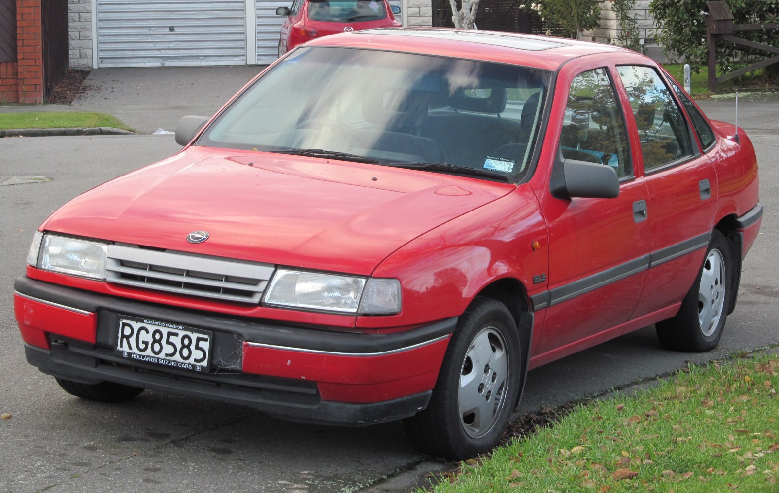 Red sedan front side with rectangular headlights and classic grille.
