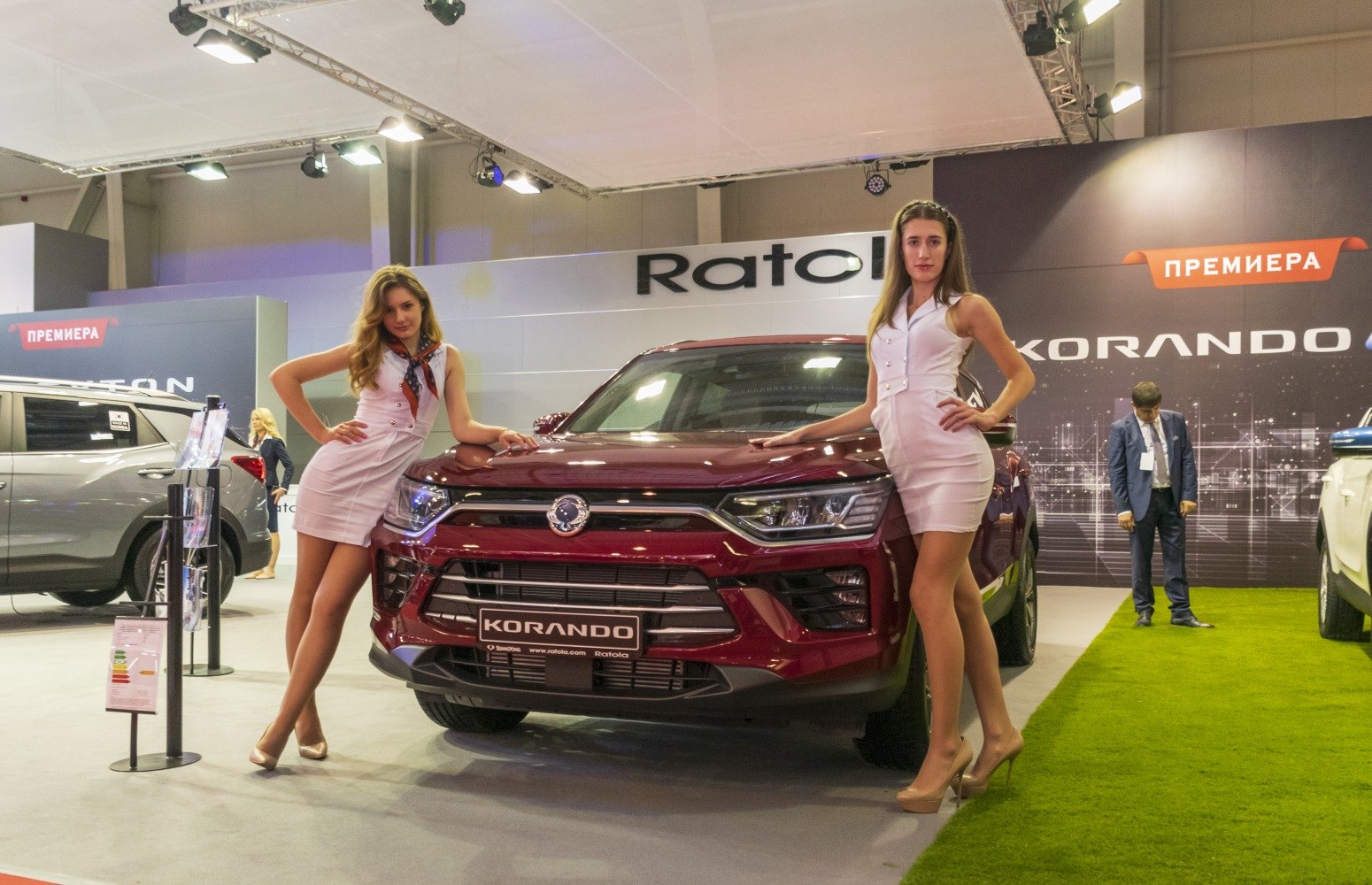 Front view of an SUV with prominent grill and headlights, flanked by two models in white dresses.