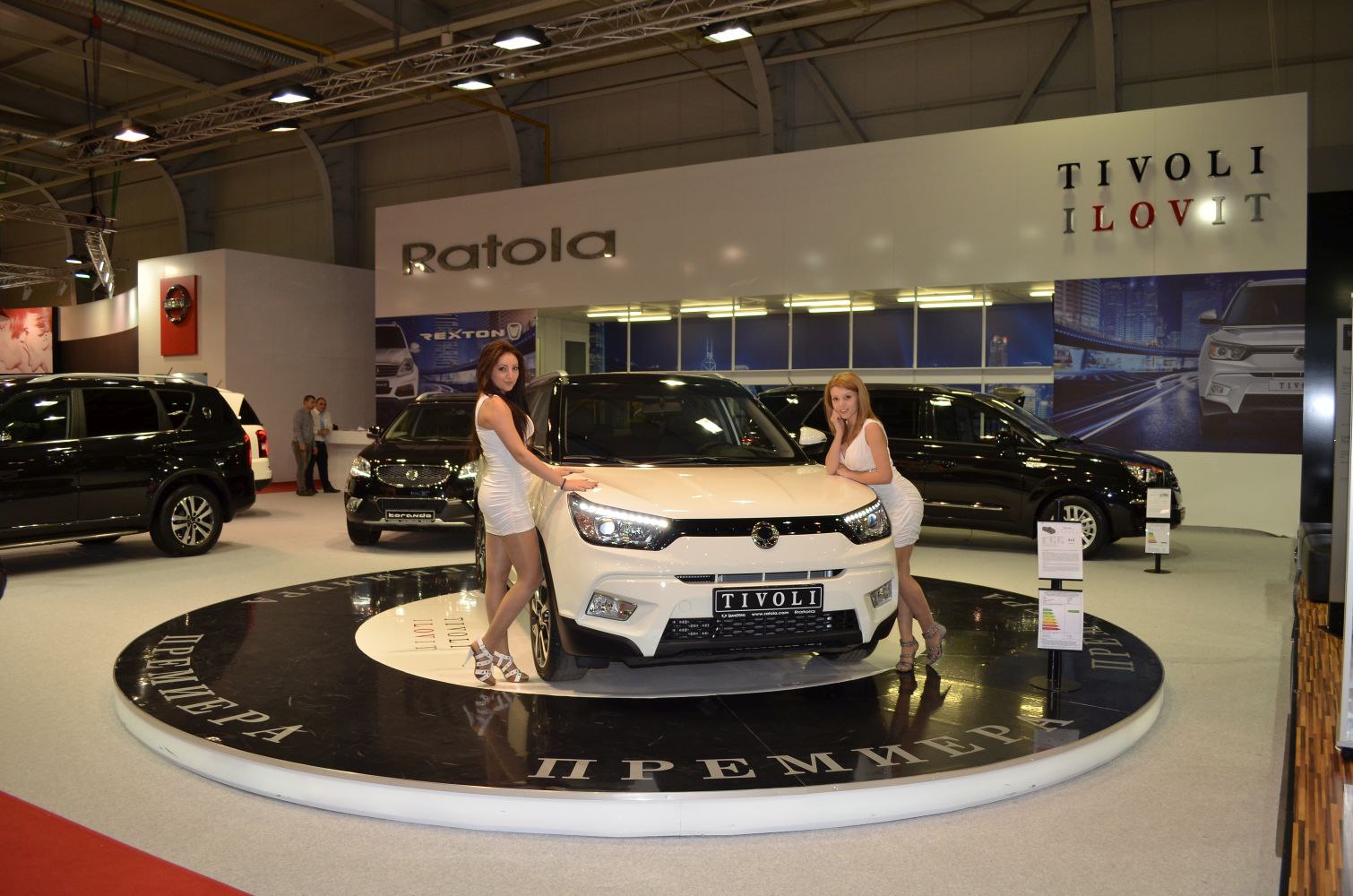 Front view of a compact SUV with illuminated headlights and models on display stand.