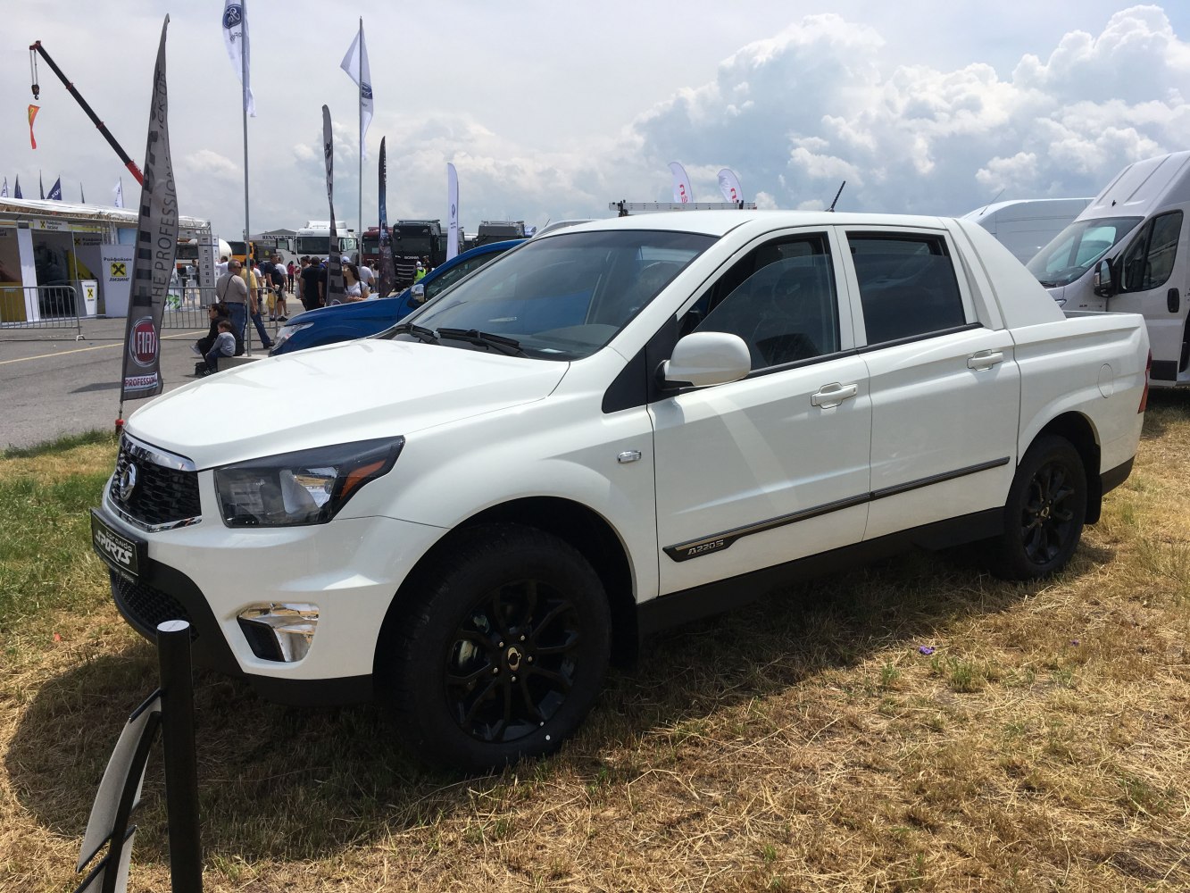 White double cab pickup with black wheels on grass at outdoor event