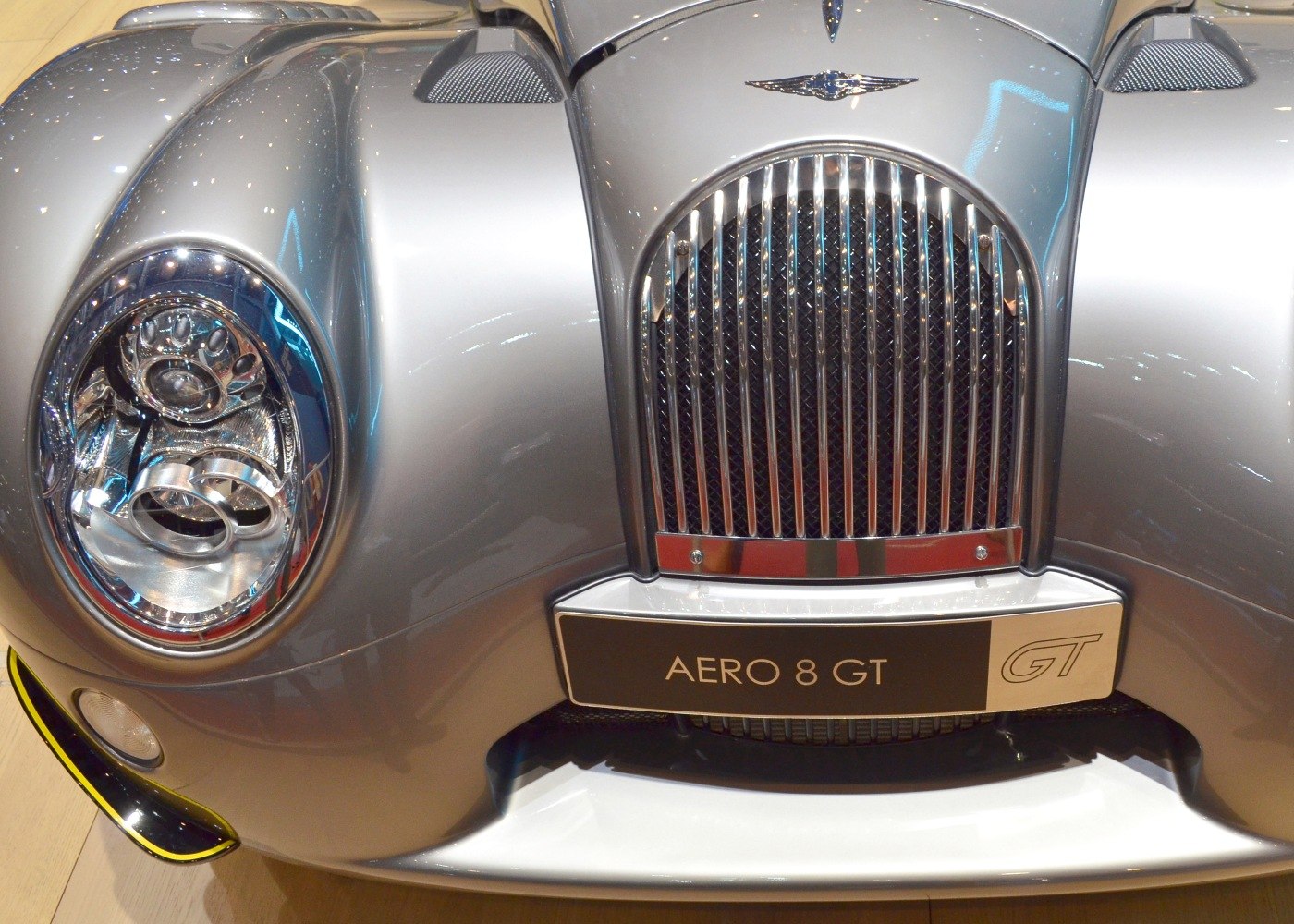 Classic front grille and modern headlight of a silver sports vehicle.