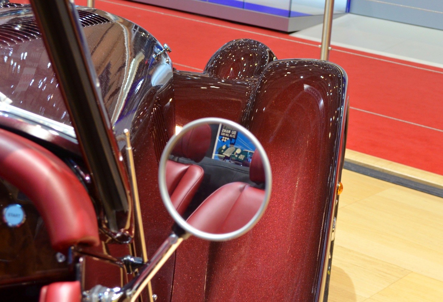 Side mirror reflecting red leather seats and shiny metallic fender