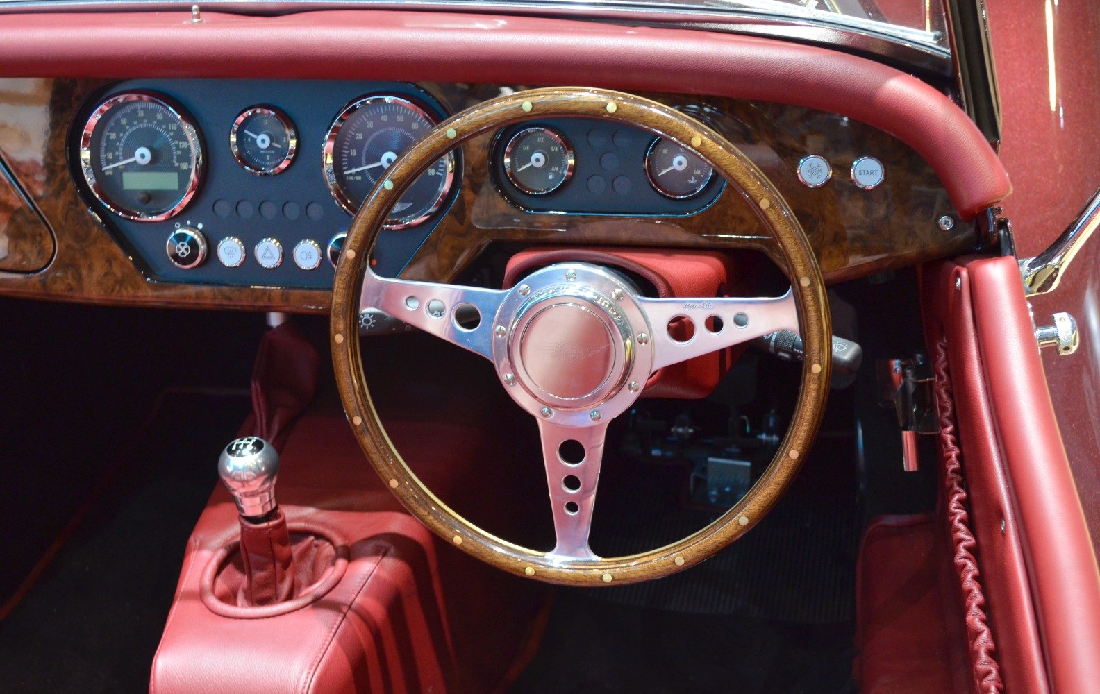 Classic wooden steering wheel and dashboard gauges in red leather interior